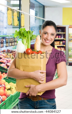 Young woman holding a grocery bag full of fresh and healthy food in a supermarket