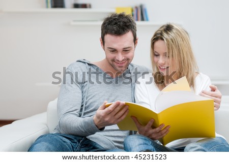 Young couple reading together a magazine in their living room at home