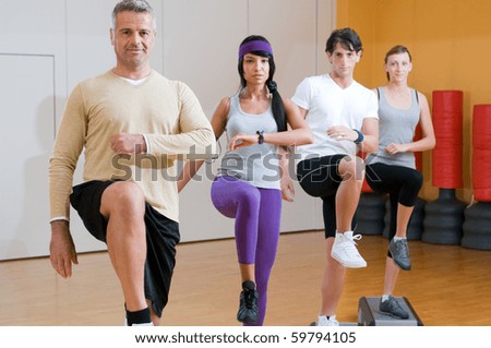 Group of healthy people with instructor doing aerobic exercises with step at gym