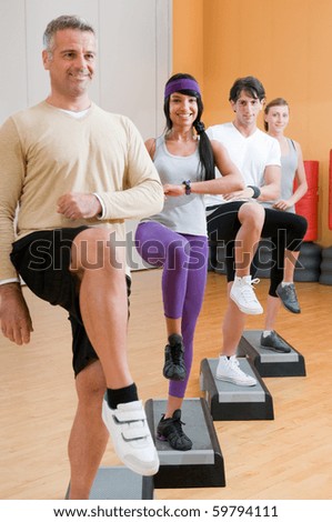 Group of healthy people with instructor doing aerobic exercises with step at gym
