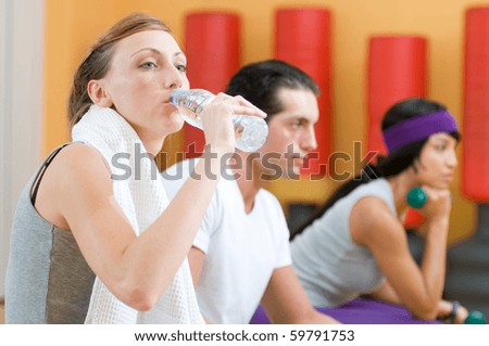 Beautiful young lady drinking bottle of water during a break at gym