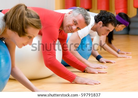 Fitness class lying on front on fitness balls at gym, mature instructor in the centre