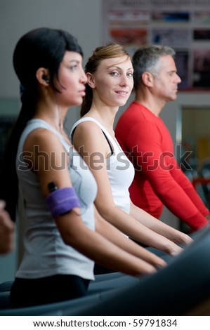 Young woman smiling at camera while walking on a treadmill at gym