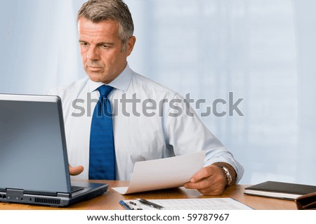 Mature businessman looking and analyzing document in his modern office at work