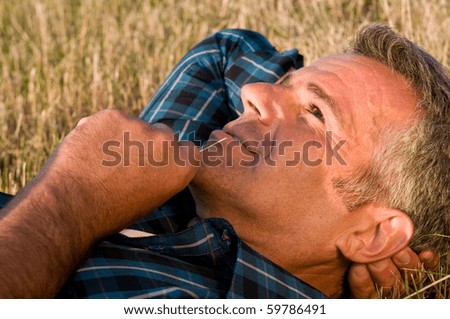 Happy smiling mature man lying down on a meadow and dreaming at his future