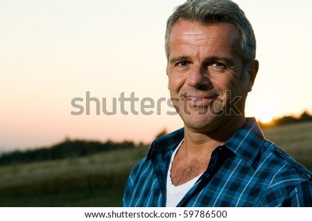 Happy smiling mature man looking at camera outdoor in a meadow