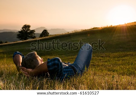 Mature man taking a break and relax in a meadow in the wonderful warm light of the sunset