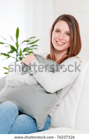 Beautiful young lady embracing a soft pillow and sitting on sofa at home