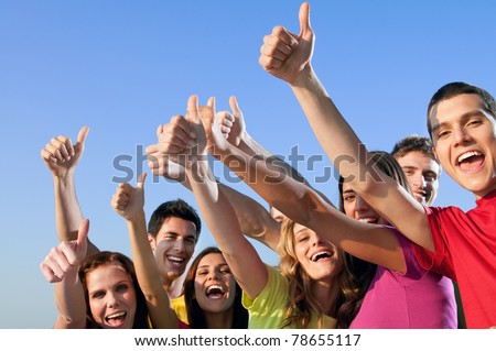 Happy group of joyful friends raising hands with thumb up sign against blue sky