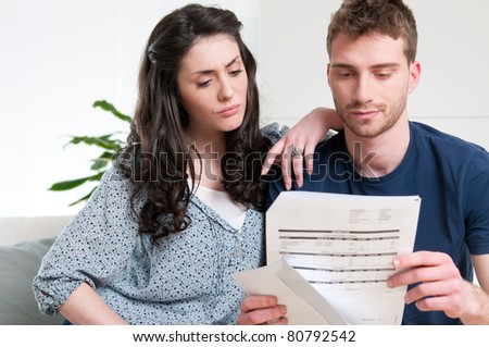 Young couple reading a financial bill or letter with worried expressions at home