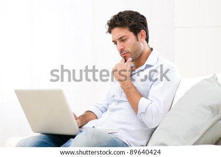 Worried young man looking at his laptop computer with pensive expression
