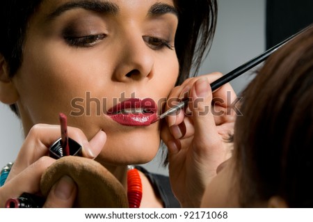 Professional makeup artist applying red lipstick on a fashion model lips before the stage