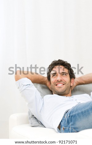 Smiling young man dreaming at his future and relaxing on sofa at home