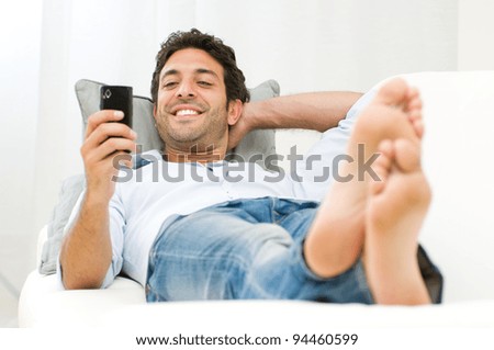 Young smiling man surfing the net and text messaging with mobile phone at home