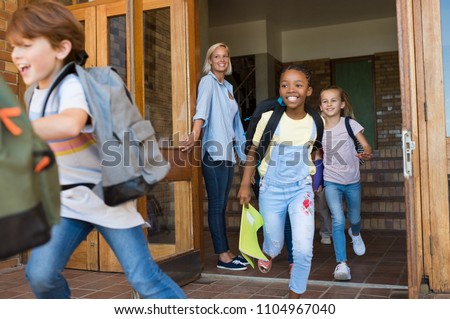Group of elementary school children running outside at the end of the lessons. Happy school boys and girls running outside from school building. Finish school and summer vacation concept.