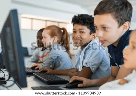 Multiethnic school kids using computer in classroom at elementary school. Portrait of arab boy looking at camera in a computer room. Smiling primary student in a row using desktop pc in class room.