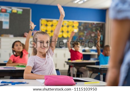 Multiethnic group of young school children raising their hands to answer a question posed by the teacher. Group of elementary kids sitting in classroom. Clever girl raising hand knowing the answer.