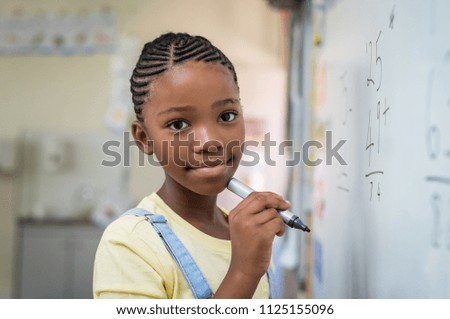 African student girl doing math problems on white board. Portrait of black schoolgirl doing math addition at whiteboard in classroom. Closeup face of schoolgirl looking at camera.