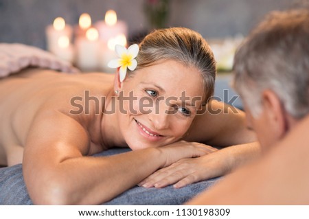 Smiling couple lying naked on massage table at spa looking at each other. Happy senior couple enjoying vacation after retirement in resort. Senior couple feeling romantic in a luxury hotel.