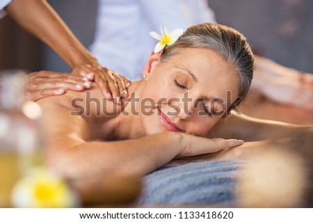 Woman lying on a spa bed and getting a relaxing massage. Serene mature woman having oil massage on her back. Portrait of senior woman with closed eyes having spa treatment.