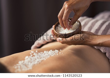 Masseuse hands doing massage on woman\'s back at beauty salon. Beauty therapist pouring salt scrub on woman back at health spa. Scrubbing and skin care concept.