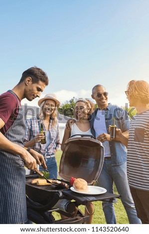 Group of multiethnic young friends enjoying barbecue in the backyard. Happy men and beautiful women talking and grilling meat. Smiling guys and girls having a good time at outdoor party.