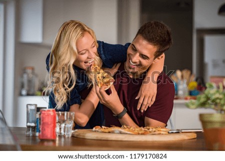 Close up of a young beautiful couple sharing pizza cut at home. Young man and happy woman sharing pizza and eating together. Handsome smiling man feeding his girlfriend with italian pizza.