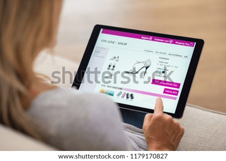 Closeup of woman doing online shopping on digital tablet at home. Rear view of woman hand touching screen while selecting shoes on ecommerce portal. Lady use e-commerce webshop to buy shoes.