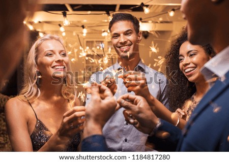 Group of multiethnic friends having fun with sparkling sticks during night party. Group of elegant women and men holding sparklers and celebrating the new year’s eve.