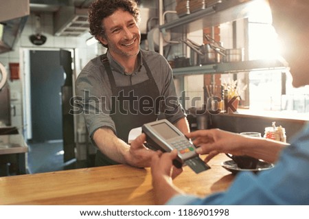 Woman paying by credit card and entering pin code on reader holded by smiling barista in cafeteria. Customer using credit card for payment. Mature cashier accepting payment over nfc technology.