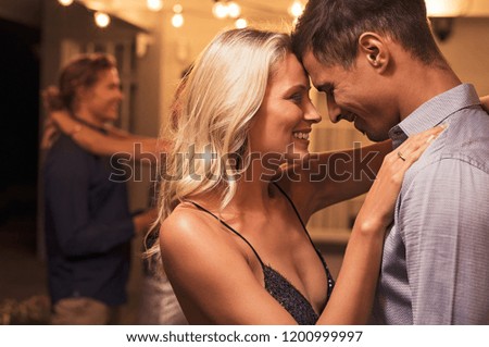 Beautiful loving couple dancing under the patio illuminated by wires of light bulbs. Young woman in love hugging her boyfriend. Romantic girl and elegant guy embracing outdoor at party night.