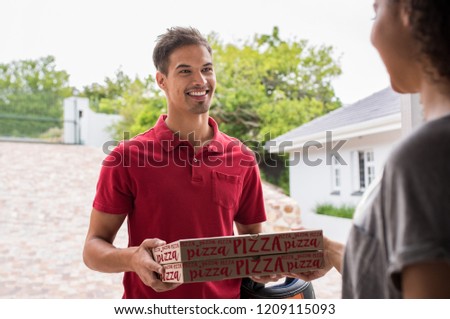 Smiling delivery boy in red t-shirt delivering two pizza boxes to woman. Happy young delivery man giving pizza to customer on the doorstep. Smiling woman receiving take away food from deliveryman.