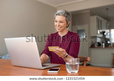 Happy senior woman making online payments of bill using laptop. Smiling mature woman shopping online with credit card. Pensioner holding credit card for internet banking and typing security code.