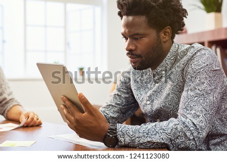 African american entrepreneur using digital tablet in his studio. Concentrated businessman working on digital tablet in a creative agency. Black casual man checking email on laptop sitting at desk.