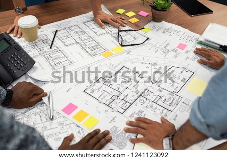 Closeup of multiethnic hands on blueprints at architects office. Team of designer and engineers working together on new residence complex. Top view of blue prints layout of house on wooden table.