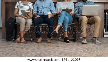 Multiethnic business people sitting on chair in a row for recruitment. Man and woman sitting while using laptop and tablets. Businessmen and casual businesswomen waiting in queue for job interview.