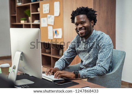 Successful african american businessman using computer at modern office. Portrait of happy creative business man feeling successful after receiving approval mail from client.