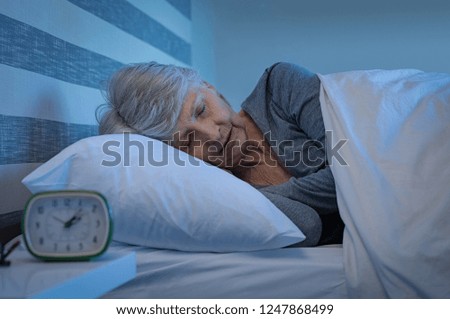 Old woman in grey hair sleeping peacefully at night time in bed. Senior woman lying on side and sleeping at home. Mature woman feeling relaxed at home while sleeping at night.