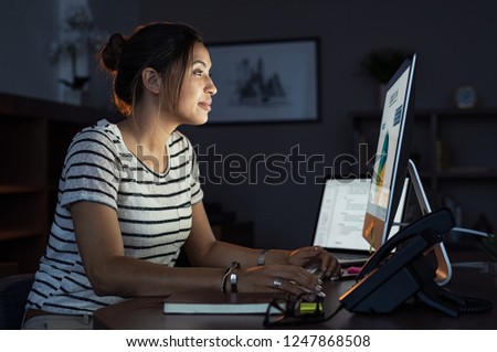 Young businesswoman in casual clothing working on desktop computer making business plan. Beautiful tired business woman working on assignment at night. Girl using computer late at night in office.