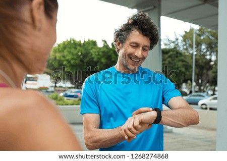 Mature jogger checking time on smart watch during running exercise. Smiling runner looking at smartwatch, checking gps position map. Happy fitness man checking heart rate monitor on wrist.