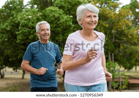 Senior couple running outside at park. Elderly man and old woman jogging together. Retired man and active woman exercising outdoor.