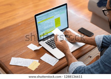 Hands of businessman analyzing invoice on laptop while checking bills. Rear view of latin man checking invoice while matching them on computer. Closeup of man hands calculating financial expenses.