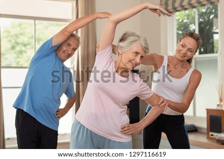 Senior couple doing exercise at home with physiotherapist. Mature gym trainer helping elderly man and old woman exercising at home. Retired husband and wife doing stretching exercises at gym.