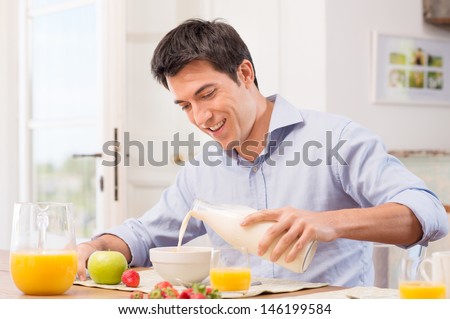 Happy Young Man Pouring Milk Into Bowl For Breakfast