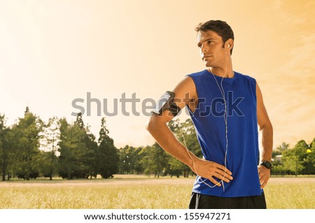 Portrait Of Male Jogger Standing In Field While Listening Music Portrait Of Male Jogger Standing In Field While Listening Music