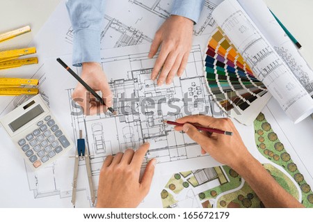 Close Up Of Two Architects Discussing Plan Together At Desk With Blueprints