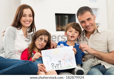 Smiling Parents With Children Sitting On Couch Showing Together Drawing of a new Home