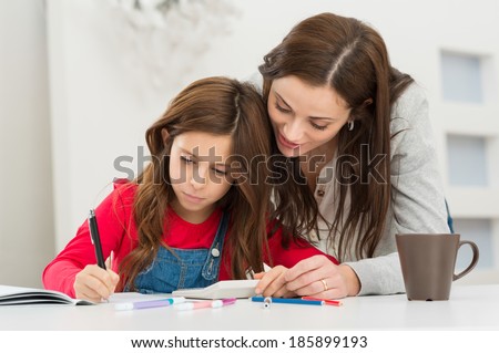 Happy Young Mother Helping Her Daughter While Studying At Home
