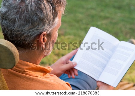 Close-up Of Mature Man Sitting On Lounge Chair Reading Book Outdoor