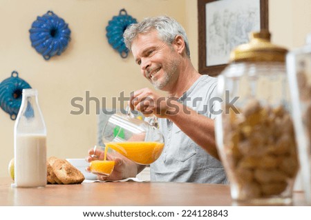 Happy Mature Man Pouring Orange Juice Into Glass For Breakfast